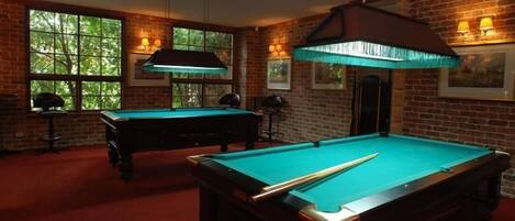 A pool table in a room with brick walls and large windows.