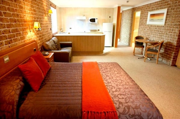 Habitación de hotel con cama, una kitchenette pequeña, zona de comedor y pared de ladrillo.