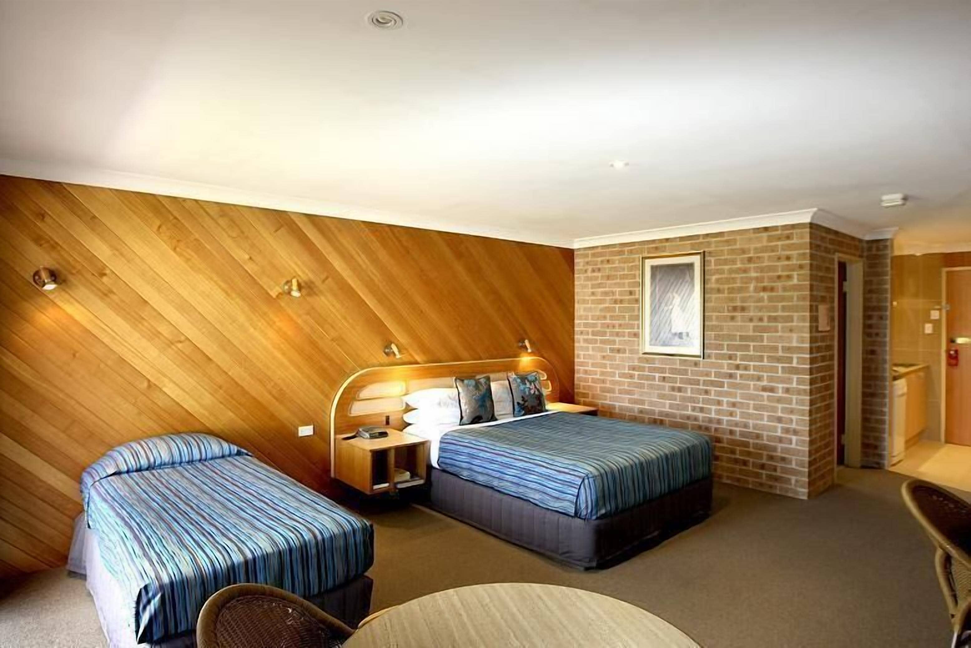 A hotel room with two beds, a wooden ceiling, a brick wall, and a small table.