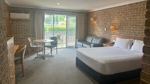 Hotellihuone, jossa on suuri sänky, työpöytä, tuoli, sohva ja parveke, jolta on näkymä ulos.