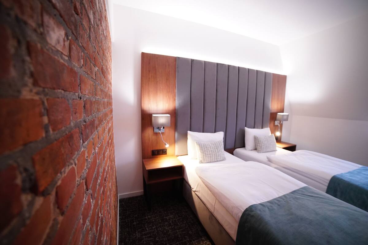 A hotel room with a brick wall, a modern headboard, two beds with white linens, and bedside lamps.