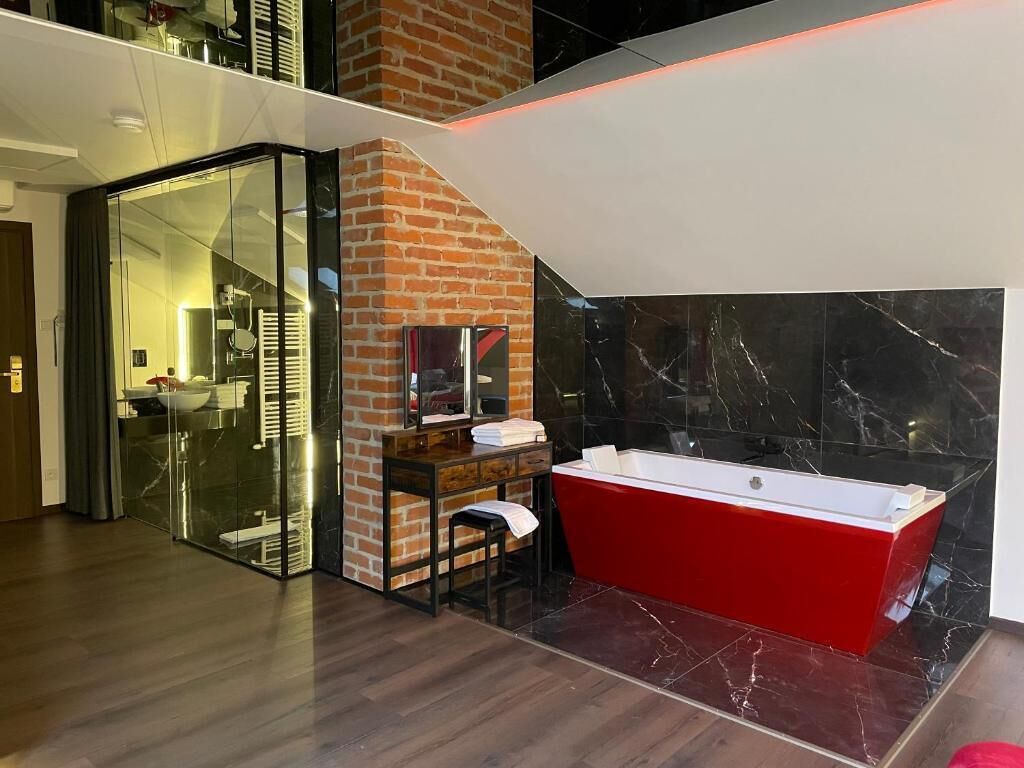 Une salle de bain moderne avec une baignoire rouge, une douche en verre et un mur d’accent en briques.