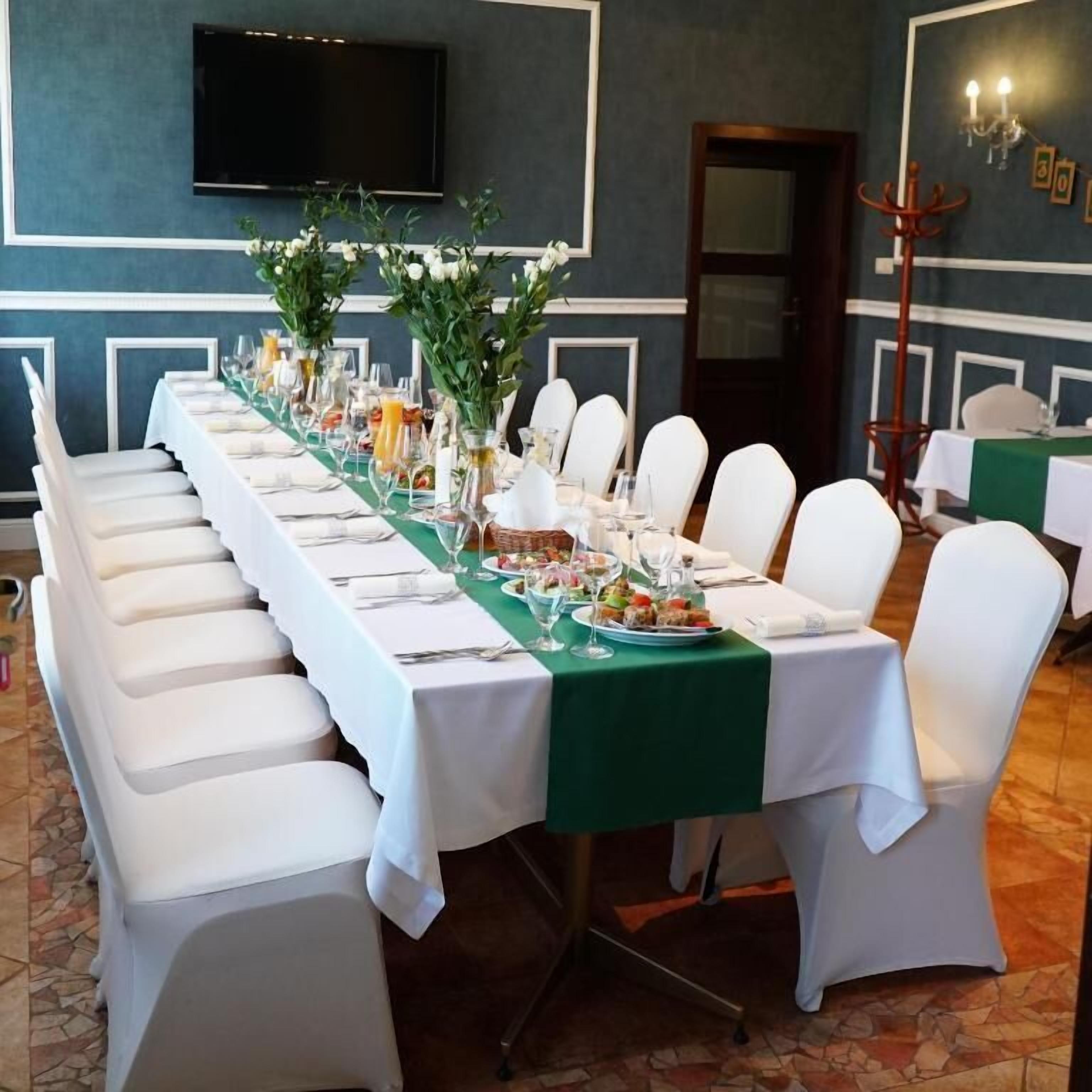 Une longue table à manger, agrémentée de chaises blanches, d’une nappe verte et de centres de table floraux.