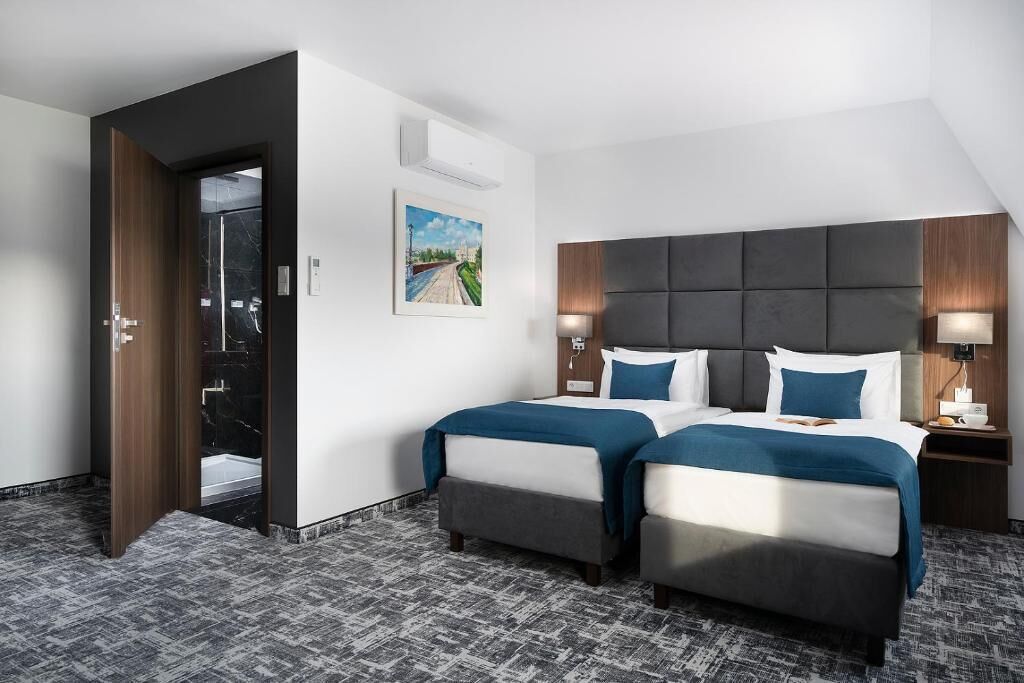 A hotel room with two beds, a large window, a painting, and a door leading to a bathroom.