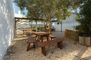 An outdoor patio with wooden tables and benches, surrounded by gravel and a white wall. -  Aldeia da Pedralva by WOT Signature (Vila do Bispo)