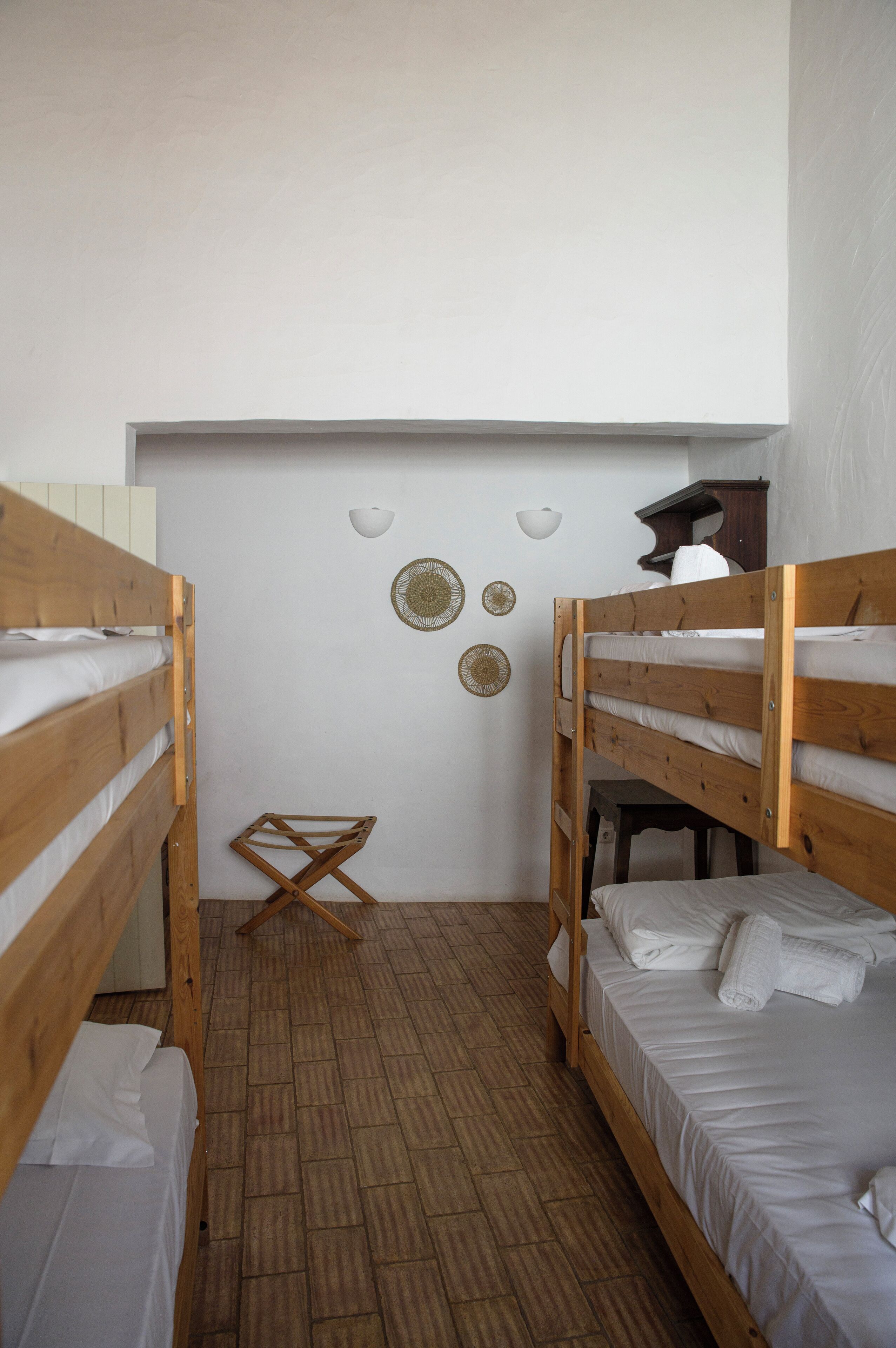 Een kleine, schone kamer met twee stapelbedden, een houten vloer en een wand versierd met decoratieve borden.
