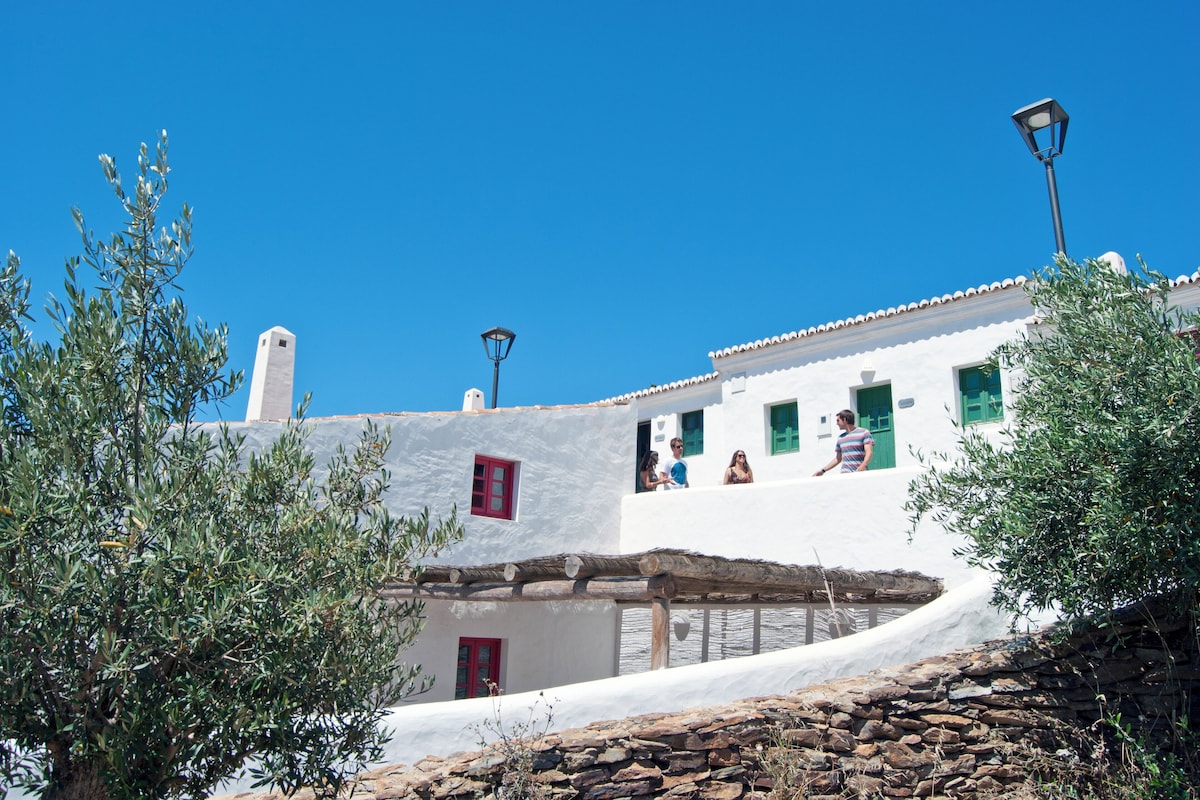 Un bâtiment blanc avec une porte rouge, un mur en pierre et un toit de chaume.