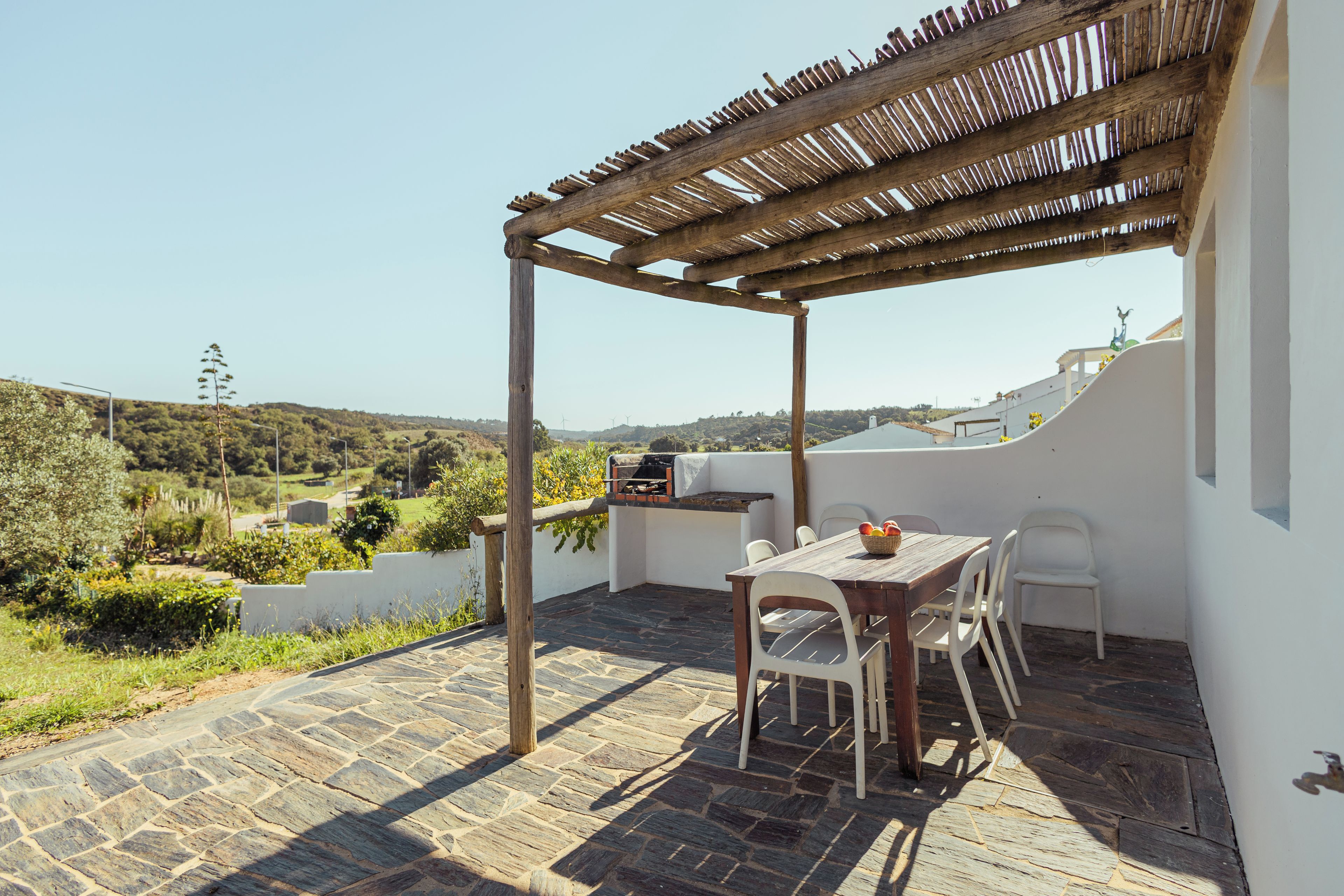 Un patio al aire libre con pérgola, piso de piedra, una parrilla y una mesa con sillas.