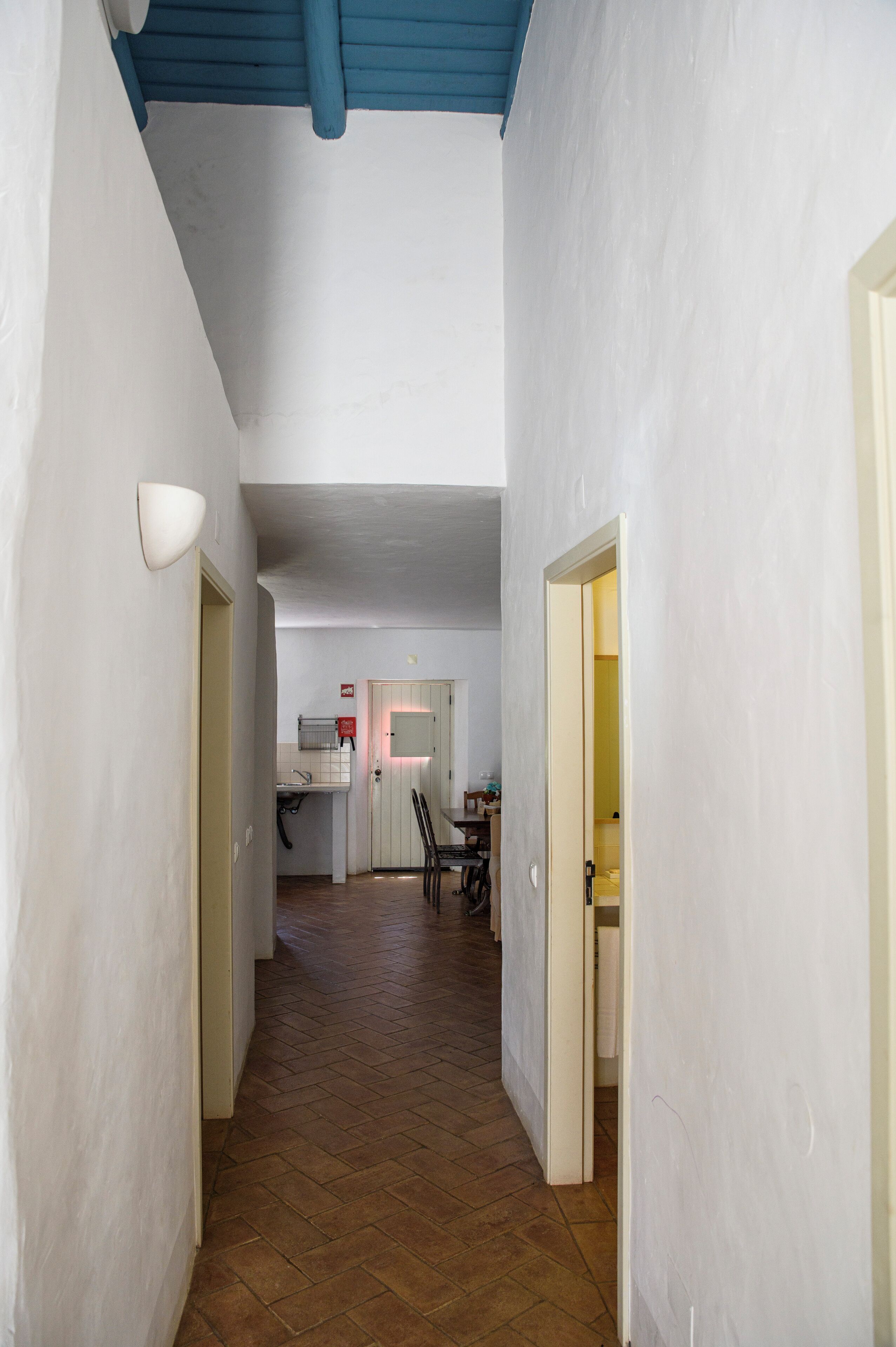 A narrow hallway with a herringbone floor leading to a kitchen area with a white countertop and a sink.
