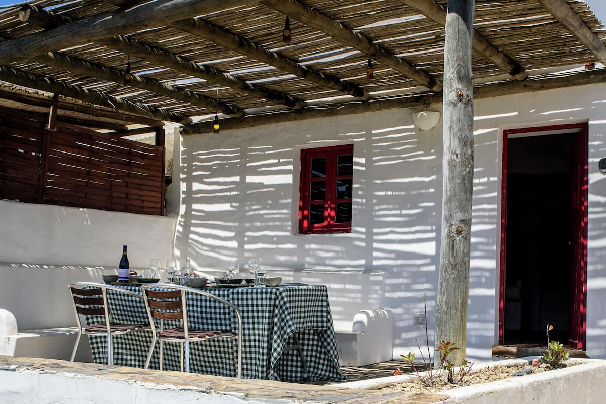 A white building with a pergola, a table with chairs, and a red door.