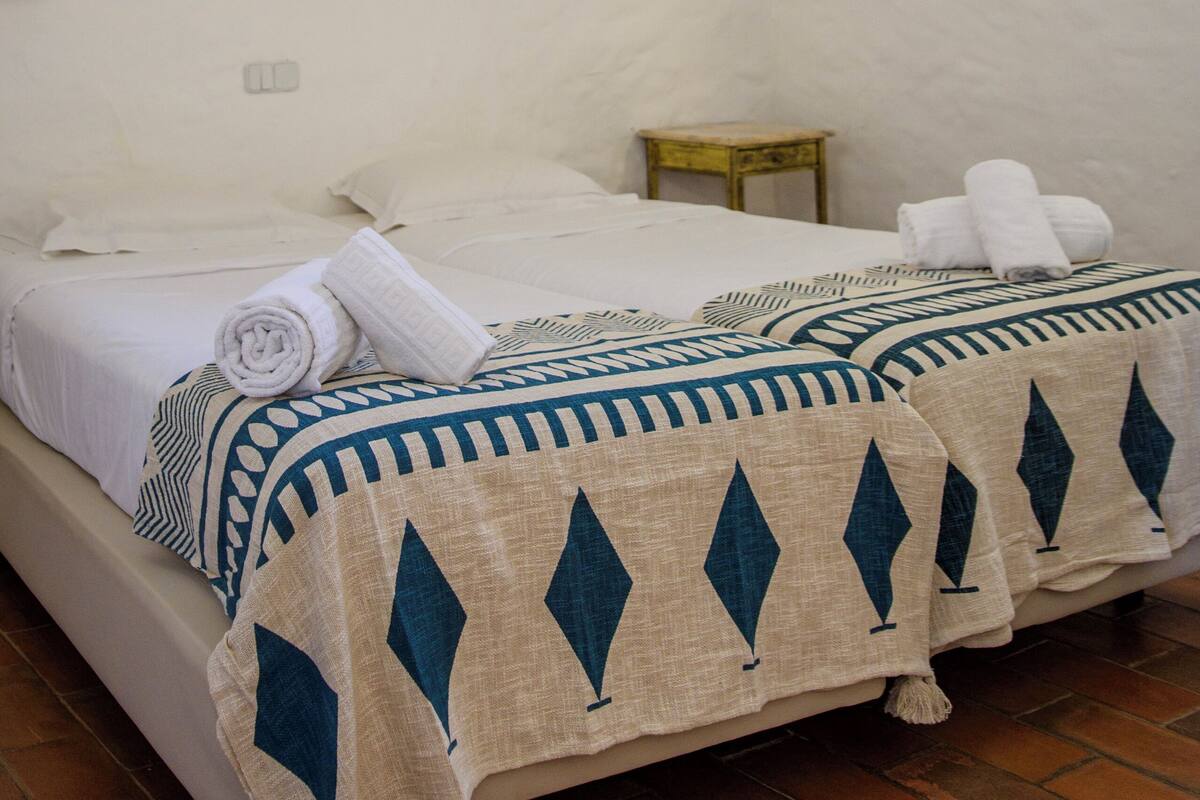 A room with two beds, a small wooden table, and wall decor.