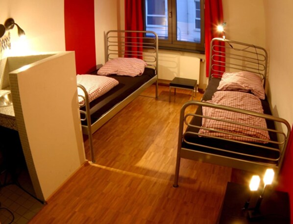 A dormitory room with two metal bunk beds, a small table, and a radiator.