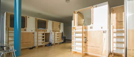 Quarto com beliches, armários individuais numerados e um pilar azul.