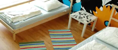 A room with a bed, a small table, and a chair. There are striped rugs on the floor.
