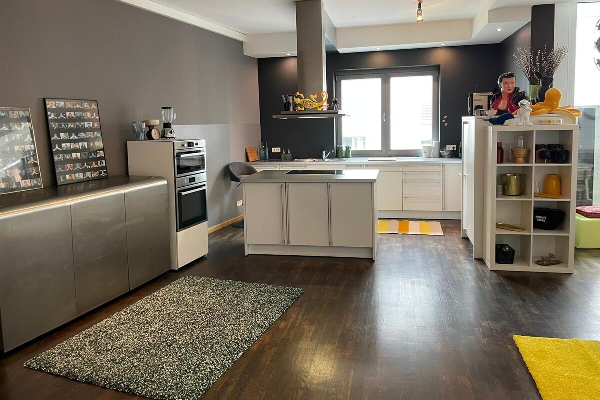 A modern kitchen with a central island, built-in appliances, and a large window providing natural light.