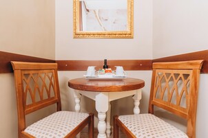 A corner room with two wooden chairs, a small round table with a tray of breakfast items, and a framed artwork on the wall.