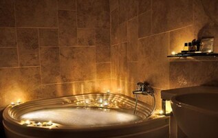 A spa area with a large oval bathtub, a sink, and a shelf with toiletries.