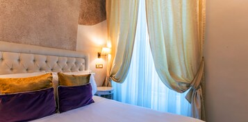 Een hotelkamer met een gestoffeerd hoofdeinde, een nachtkastje met een lamp en transparante gordijnen.