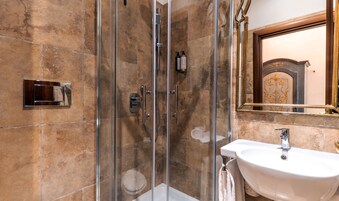 A bathroom with a glass-enclosed shower, a white sink, and a mirror with a decorative frame.