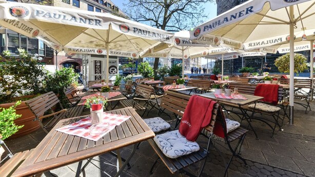 An outdoor seating area with tables and chairs, covered by umbrellas, and a building in the background. - Pillhofer Hotel (Nuremberg)