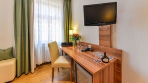 A hotel room with a wooden desk, a television mounted on the wall, a sofa, and a window with curtains. - Pillhofer Hotel (Nuremberg)