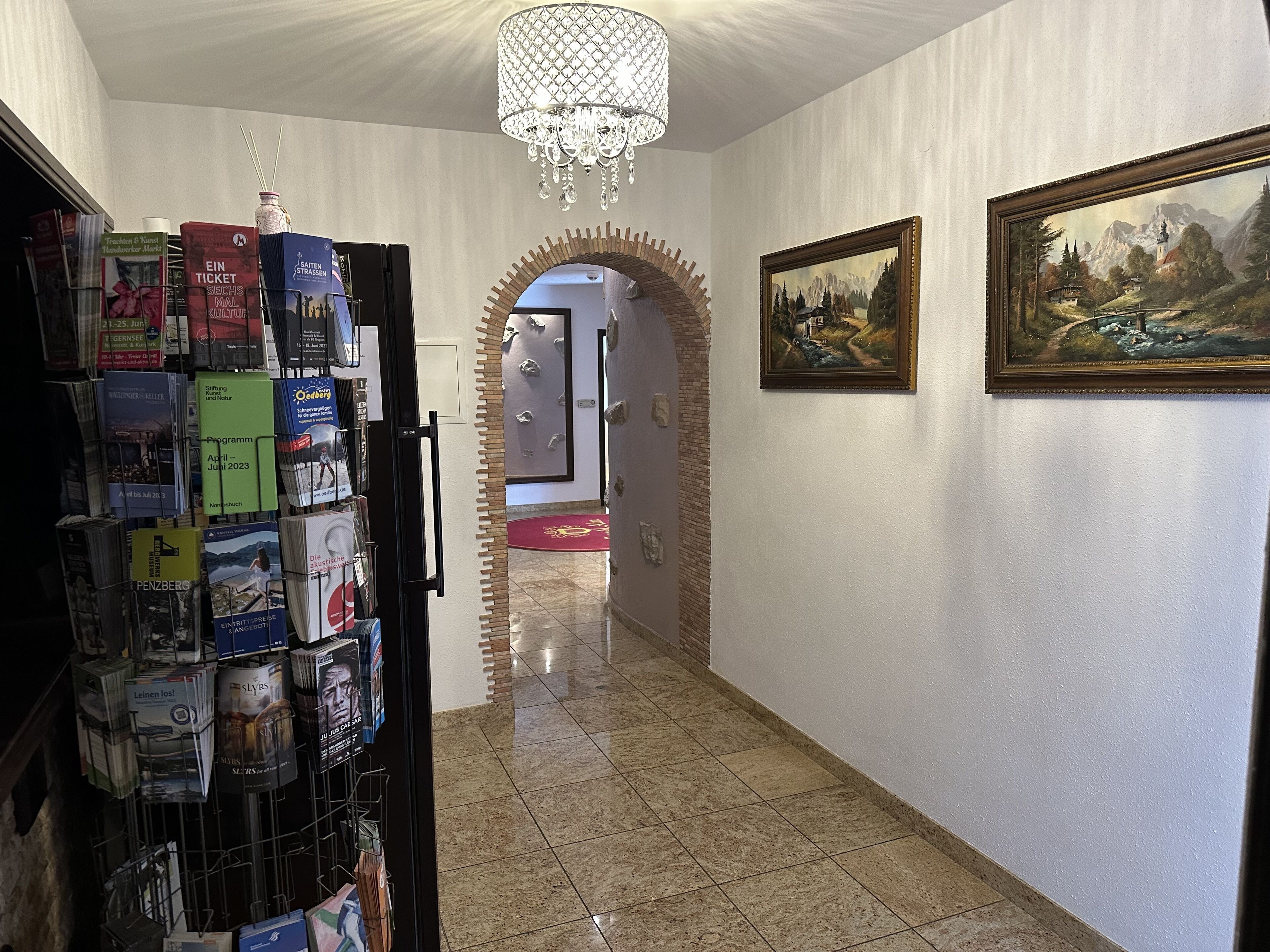 A hallway with a chandelier, a bookcase, and a framed painting.