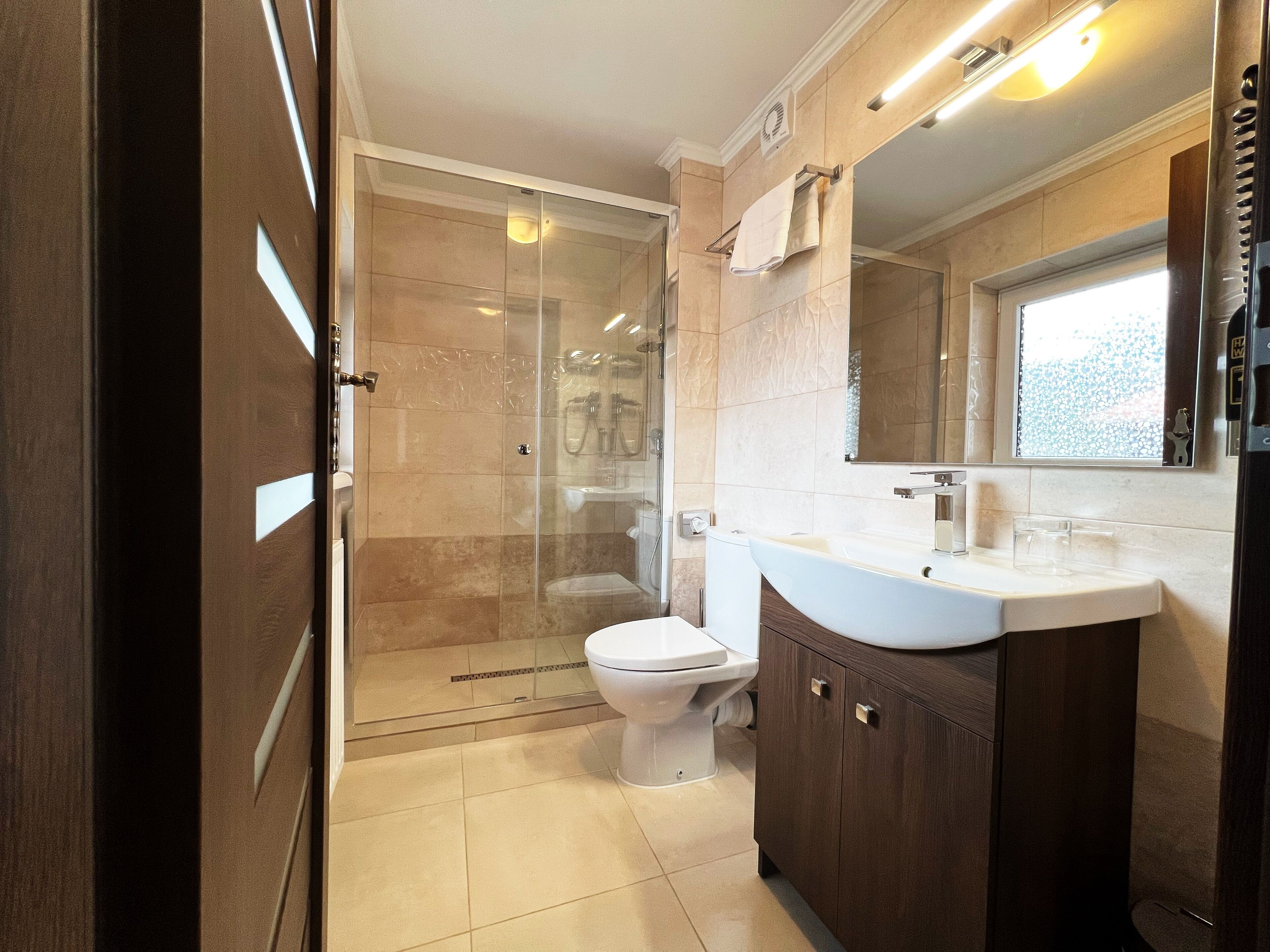Un baño moderno con ducha de vidrio, inodoro blanco y tocador de madera con espejo.