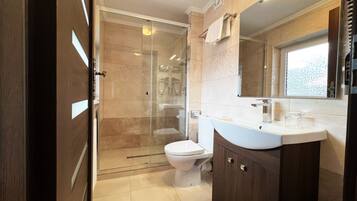 Un baño moderno con ducha de vidrio, inodoro blanco y tocador de madera con espejo.