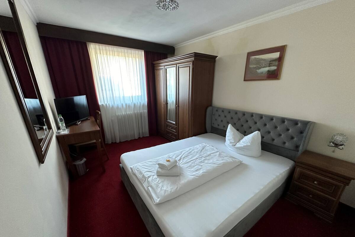 A hotel room with a bed, a desk, a television, and a wardrobe.