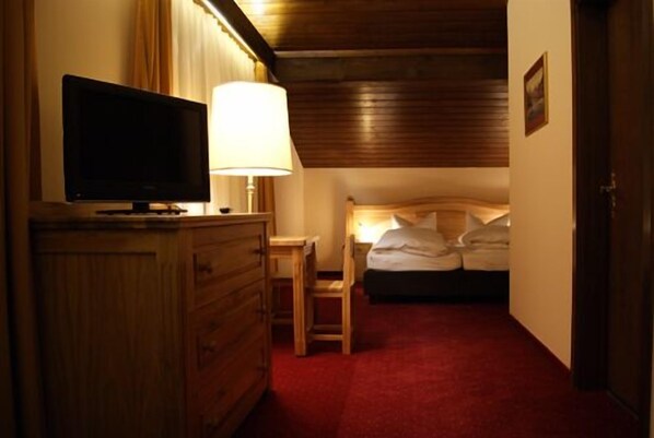 A hotel room with a wooden dresser, a television, a bedside table with a lamp, and a bed with pillows.