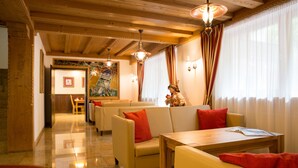 Vestíbulo de hotel con techo de madera, zona de recepción y comedor con mesas y sillas.
