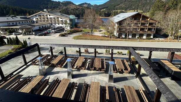 Un complejo turístico de montaña con bancos de madera, un área de estacionamiento y edificios con balcones con vistas al paisaje.