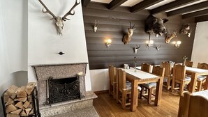 Un comedor con mesas y sillas de madera, una chimenea de piedra y cráneos de animales montados en la pared.