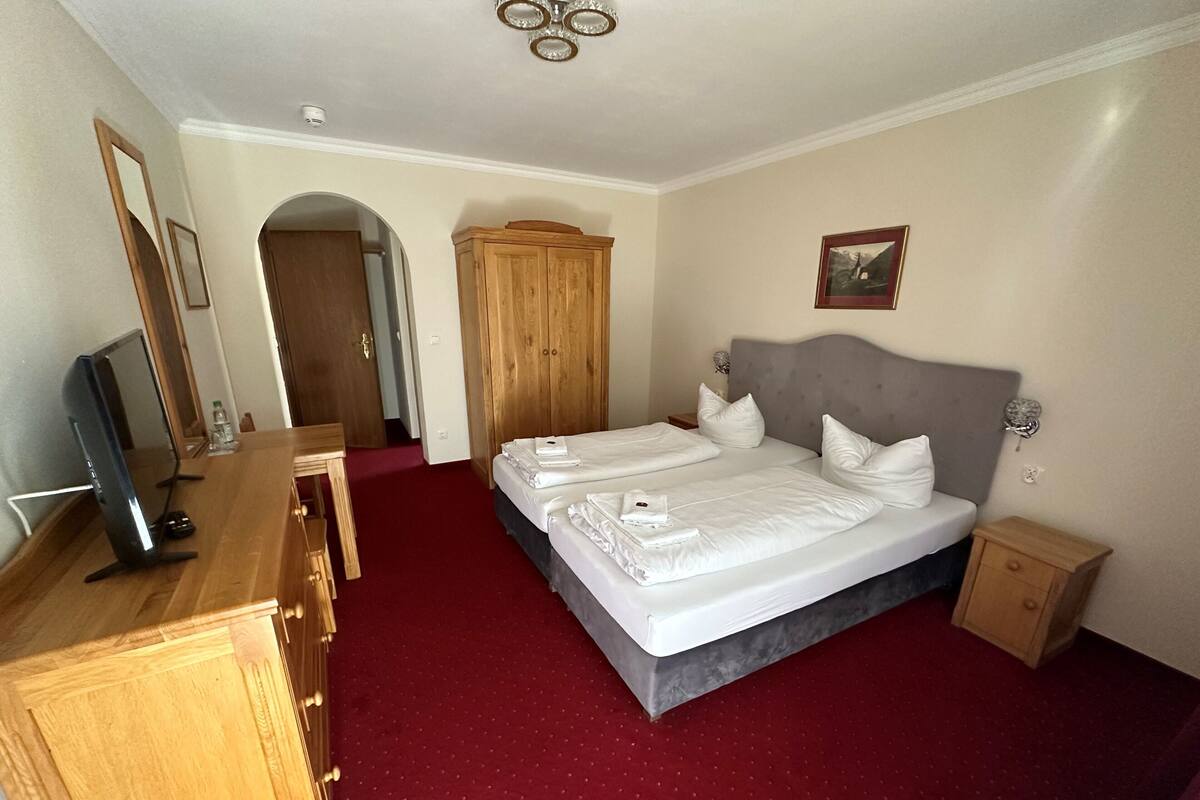 A hotel room with a large bed, a wooden wardrobe, a desk with a computer, and a TV.