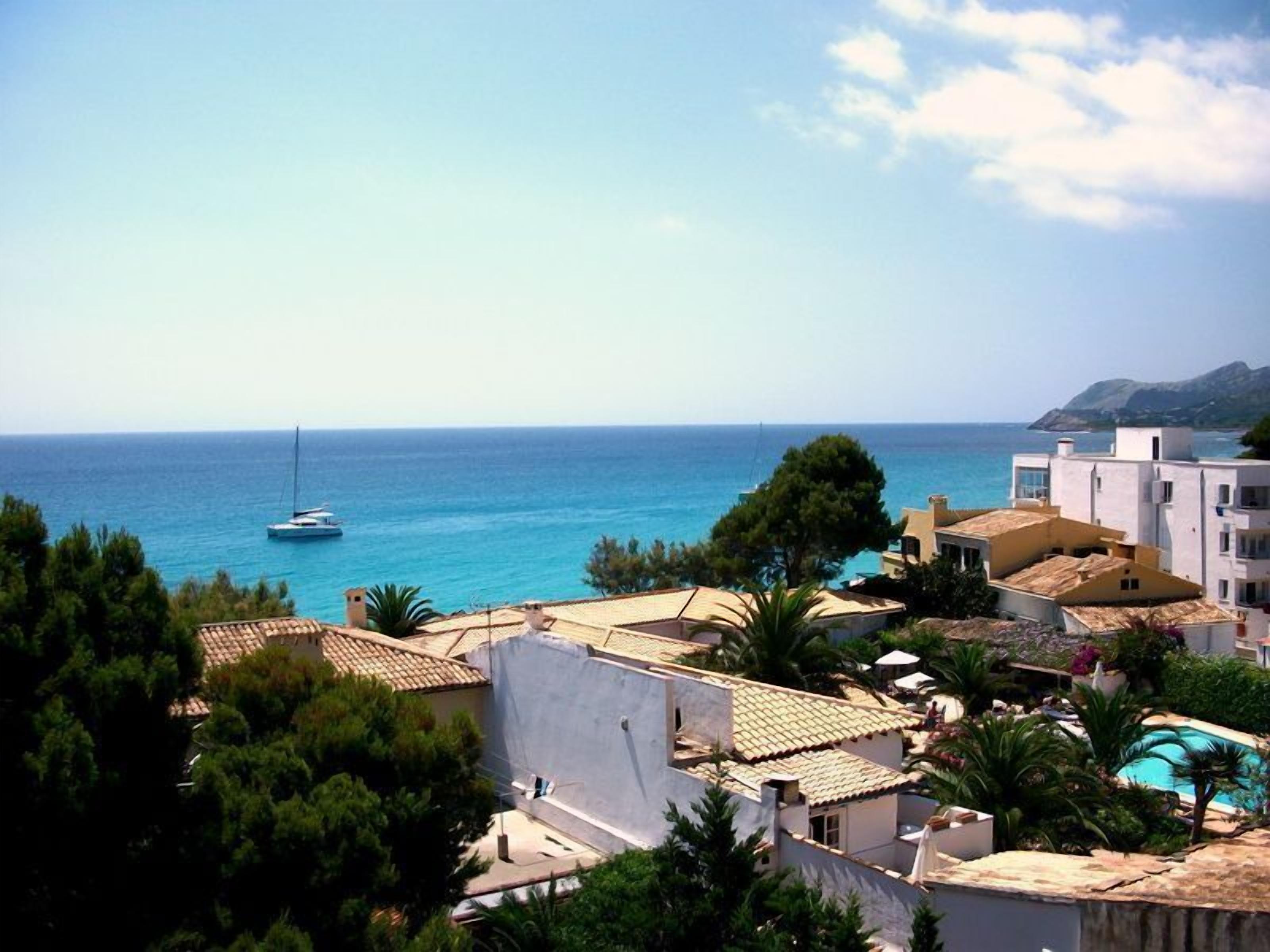 A coastal residential area with a view of the sea, a sailboat, and a swimming pool.