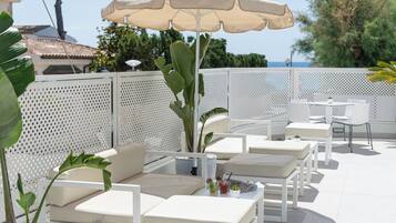 Een terras met wit meubilair, een grote parasol en uitzicht op zee.