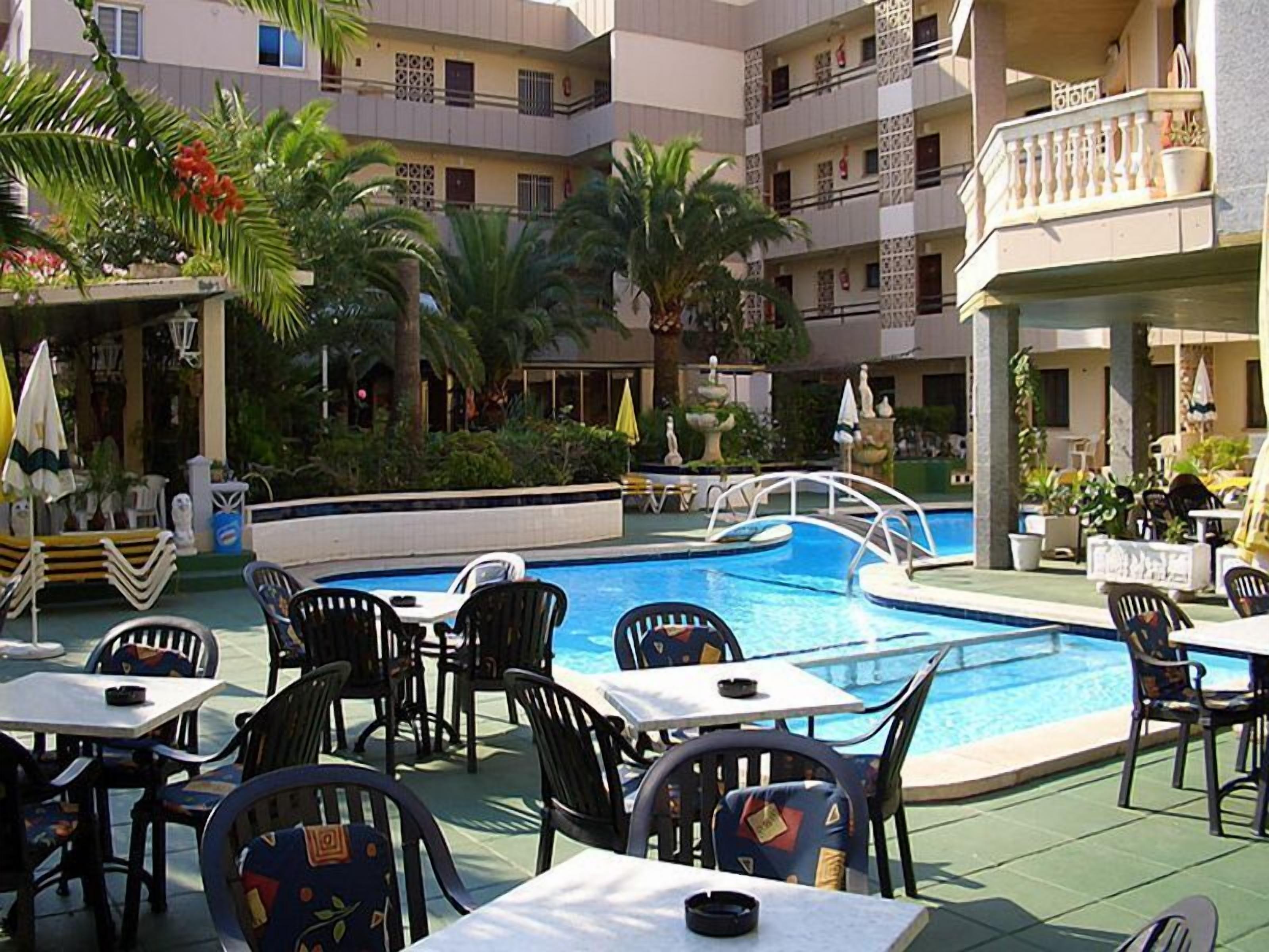 Area piscina con diversi tavoli e sedie, una piscina e vegetazione circostante.