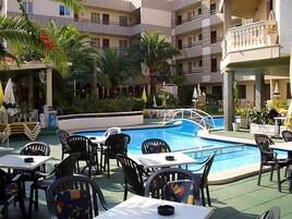 Zona junto a la piscina con varias mesas y sillas, una piscina y follaje circundante.