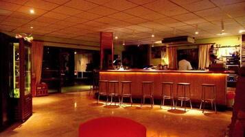 Zona de bar con taburetes, una barra y una cocina al fondo.