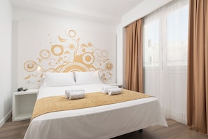 Una habitación de hotel con cama, mesita de noche, decoración en la pared y una ventana con cortinas.
