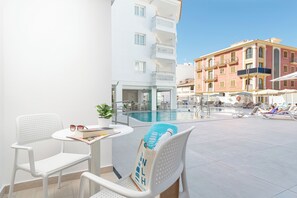 Zona de piscina con una silla blanca, una mesa con un libro y gafas de sol, y un cartel que dice 'WELKHEHOTEL'.