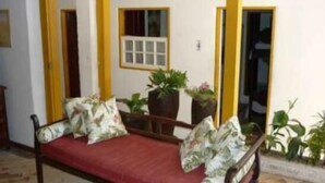 Una habitación con una cama de madera, detalles en amarillo, un ventanal y plantas en macetas.