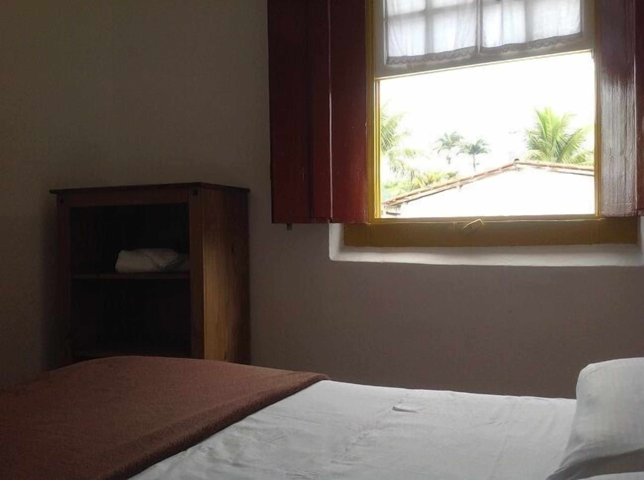 Una habitación con una cama, un armario de madera y una ventana con vistas a palmeras.