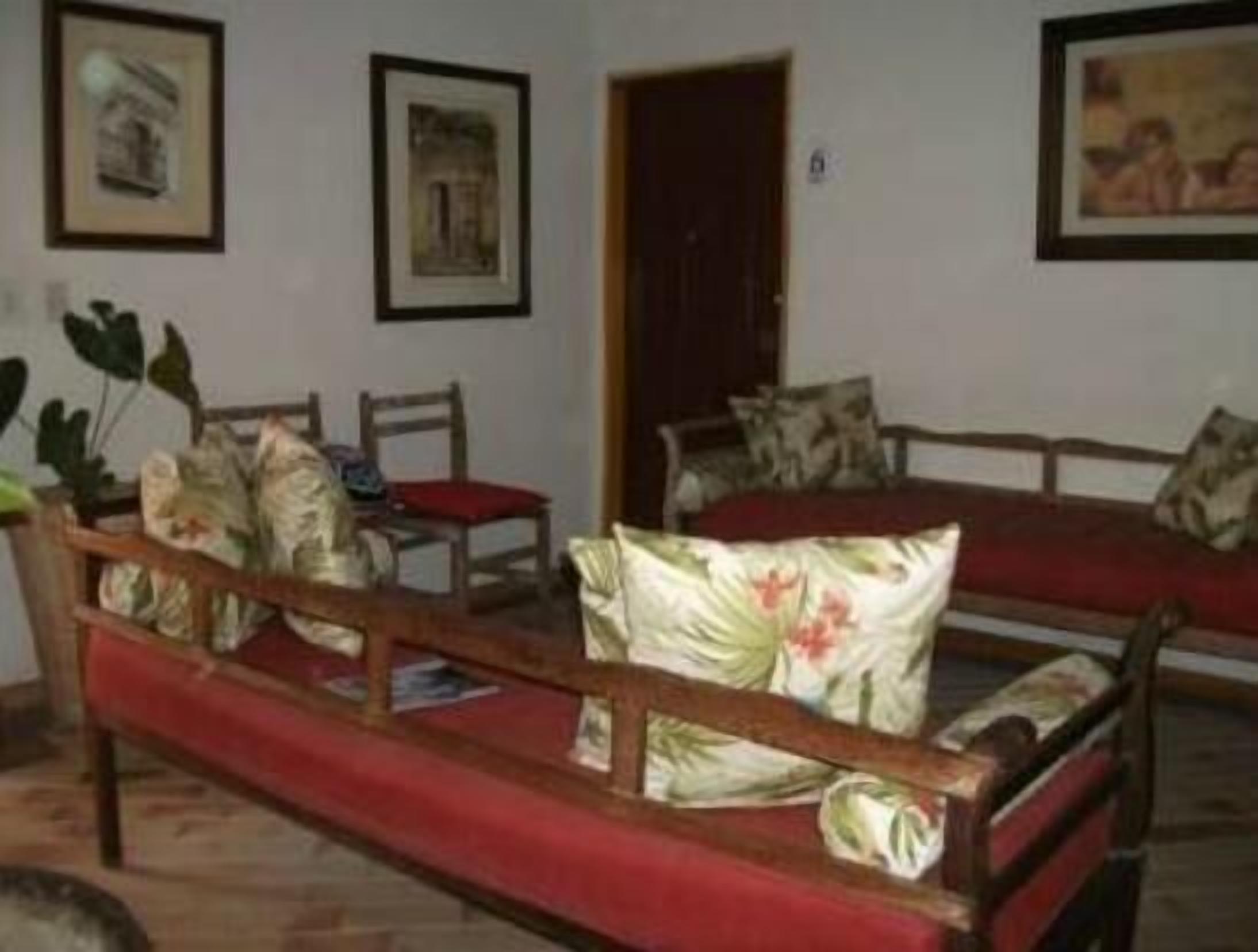 Une pièce avec un canapé rouge, une chaise en bois et une petite table. Des tableaux encadrés ornent les murs.