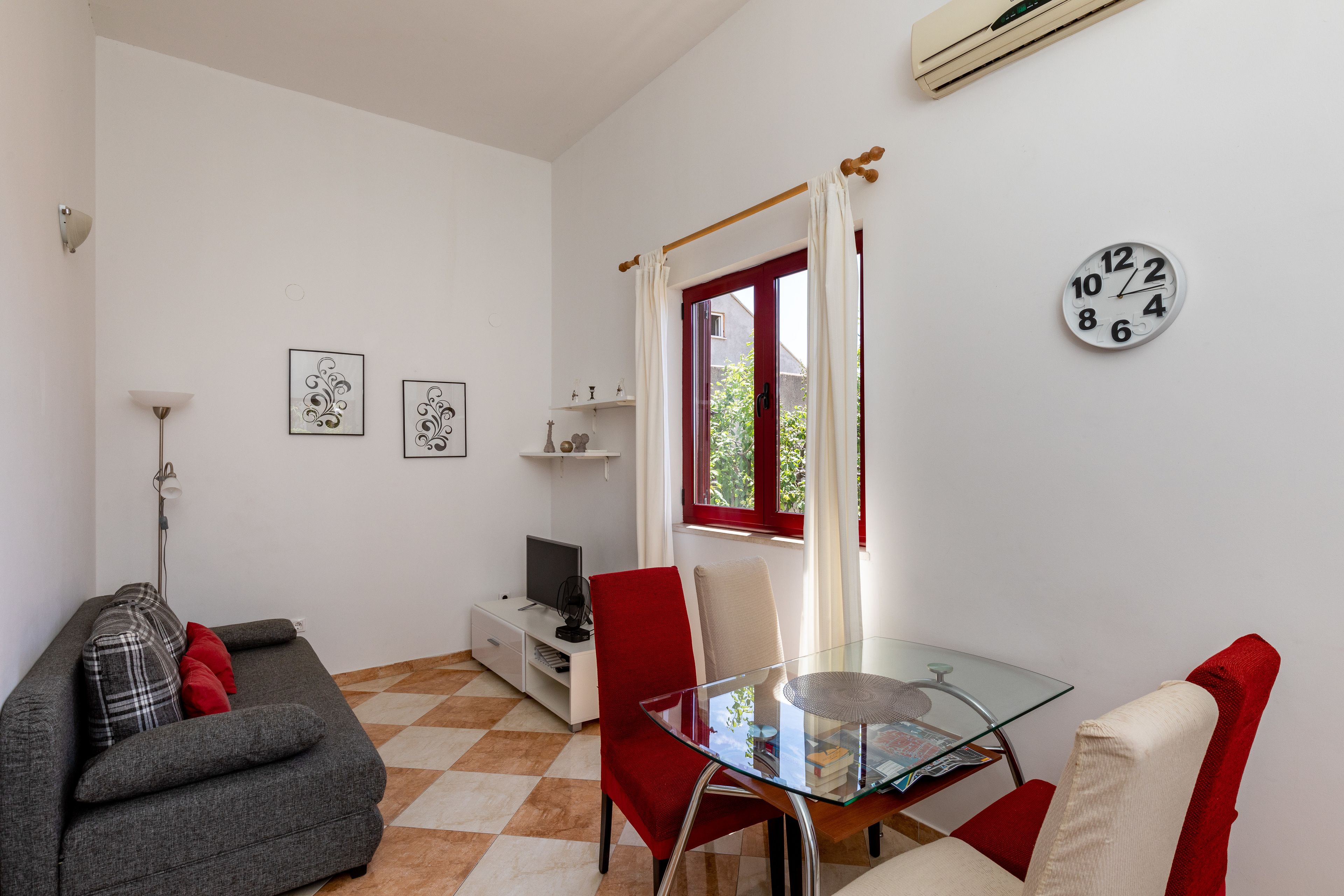 Uma sala de estar moderna com uma mesa de jantar de vidro, cadeiras vermelhas, um sofá cinza e um chão xadrez vermelho e branco.