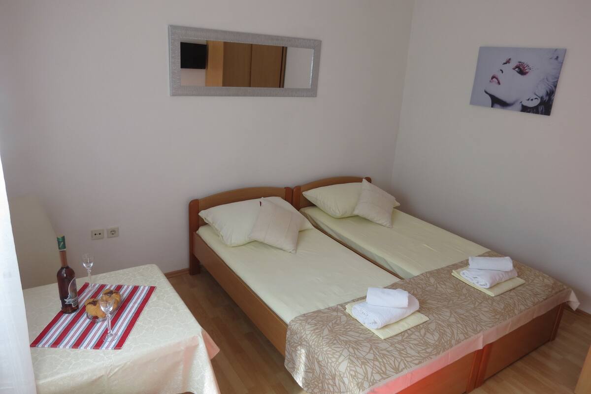 Een kamer met twee eenpersoonsbedden, een kleine tafel met een fles en glazen, en een spiegel aan de muur.
