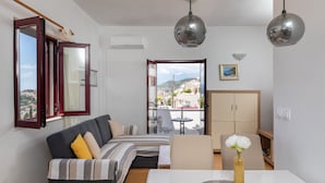 Un salon moderne avec un canapé, une table à manger agrémentée d’un vase, et une vue sur l’extérieur par une porte ouverte.