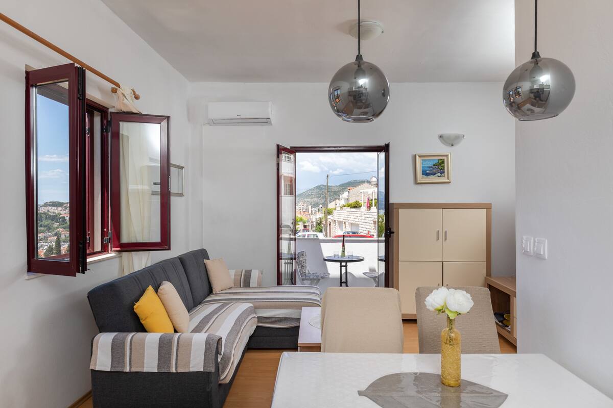 Een moderne woonkamer met een bank, een eettafel met een vaas en uitzicht door een open deur.