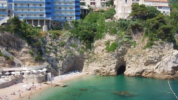 Une zone côtière avec une plage, une falaise rocheuse et des bâtiments en arrière-plan.