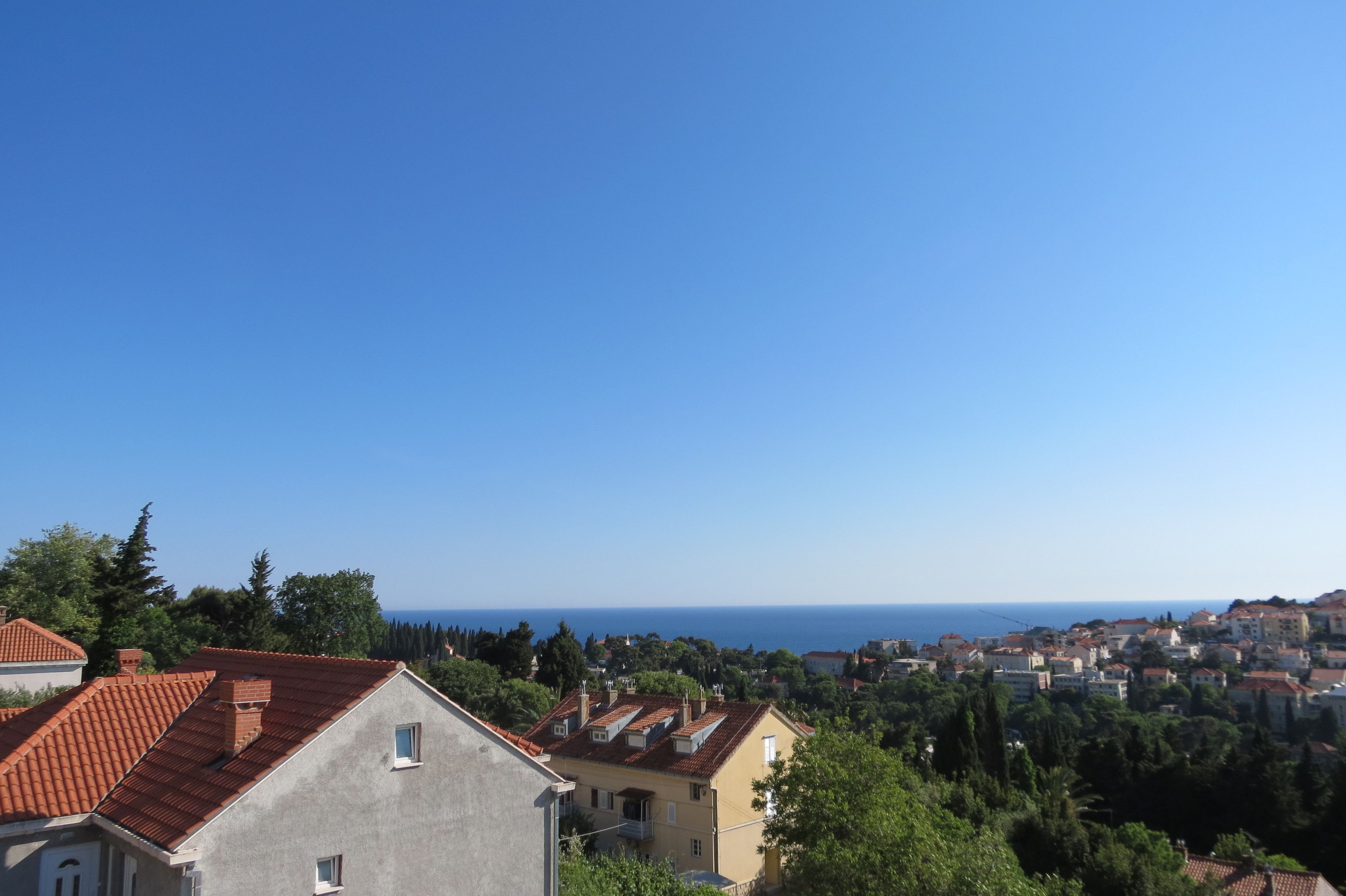 Une ville côtière aux bâtiments aux toits de tuiles rouges, à la végétation luxuriante et d’où l’on a une vue dégagée sur la mer.